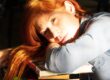 Donna con capelli rossi che riposa la testa sui libri appoggiati a un banco scolastico.