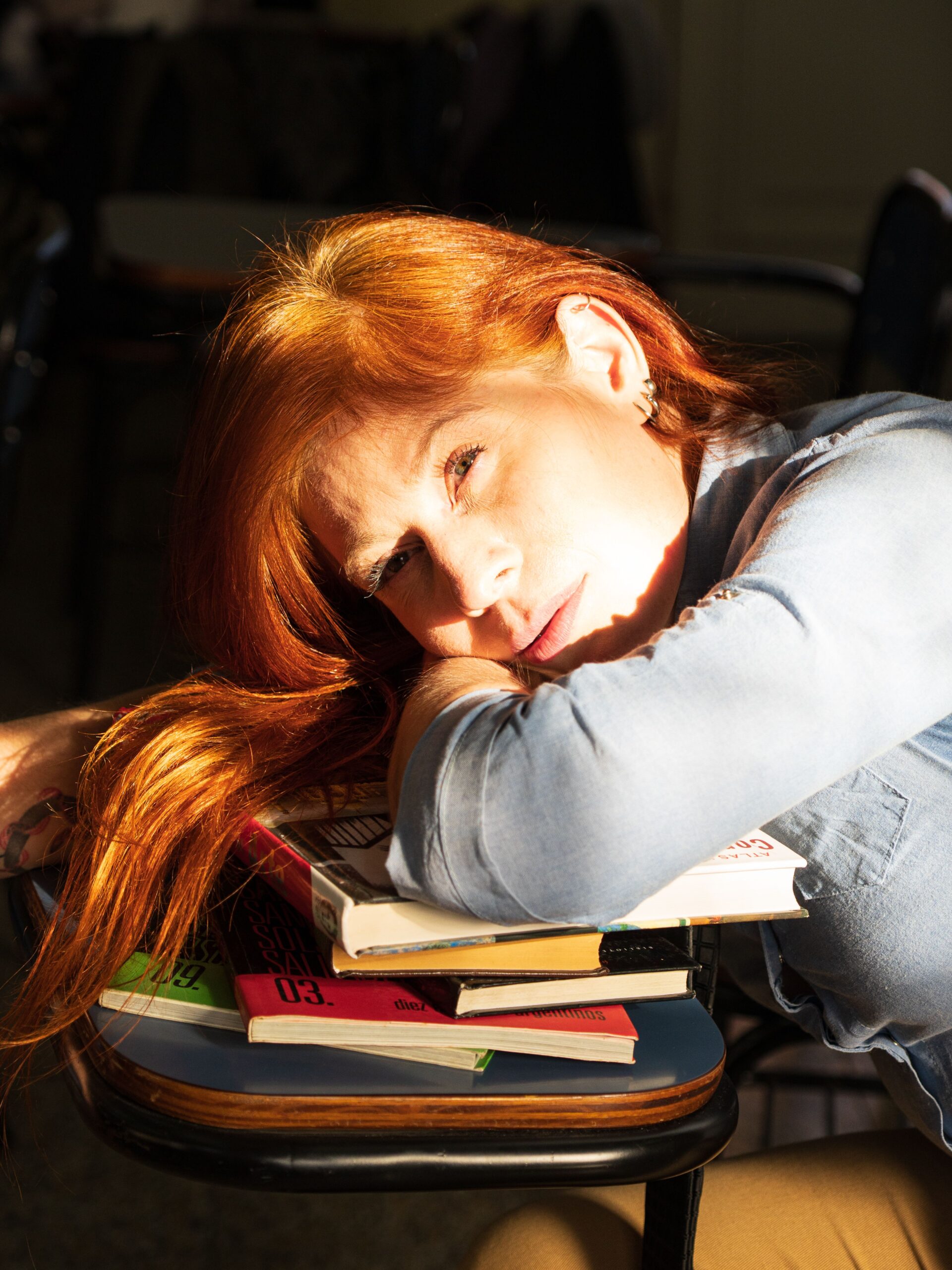 Ansia da rientro scolastico Donna con capelli rossi che riposa la testa sui libri appoggiati a un banco scolastico.
