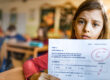 Una bambina con il volto triste mostra una verifica in cui ha preso un brutto voto.