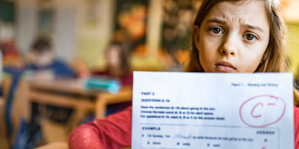 Come superare i brutti voti a scuola Una bambina con il volto triste mostra una verifica in cui ha preso un brutto voto.