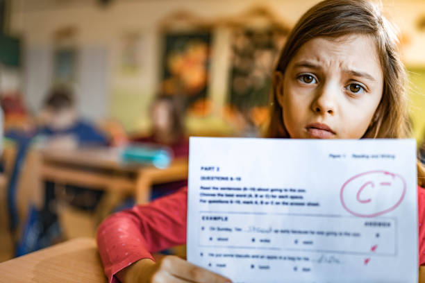 Come superare i brutti voti a scuola Una bambina con il volto triste mostra una verifica in cui ha preso un brutto voto.