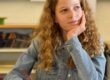 Una studentessa con i capelli rossi e ricci guarda fuori dalla finestra sorridendo.