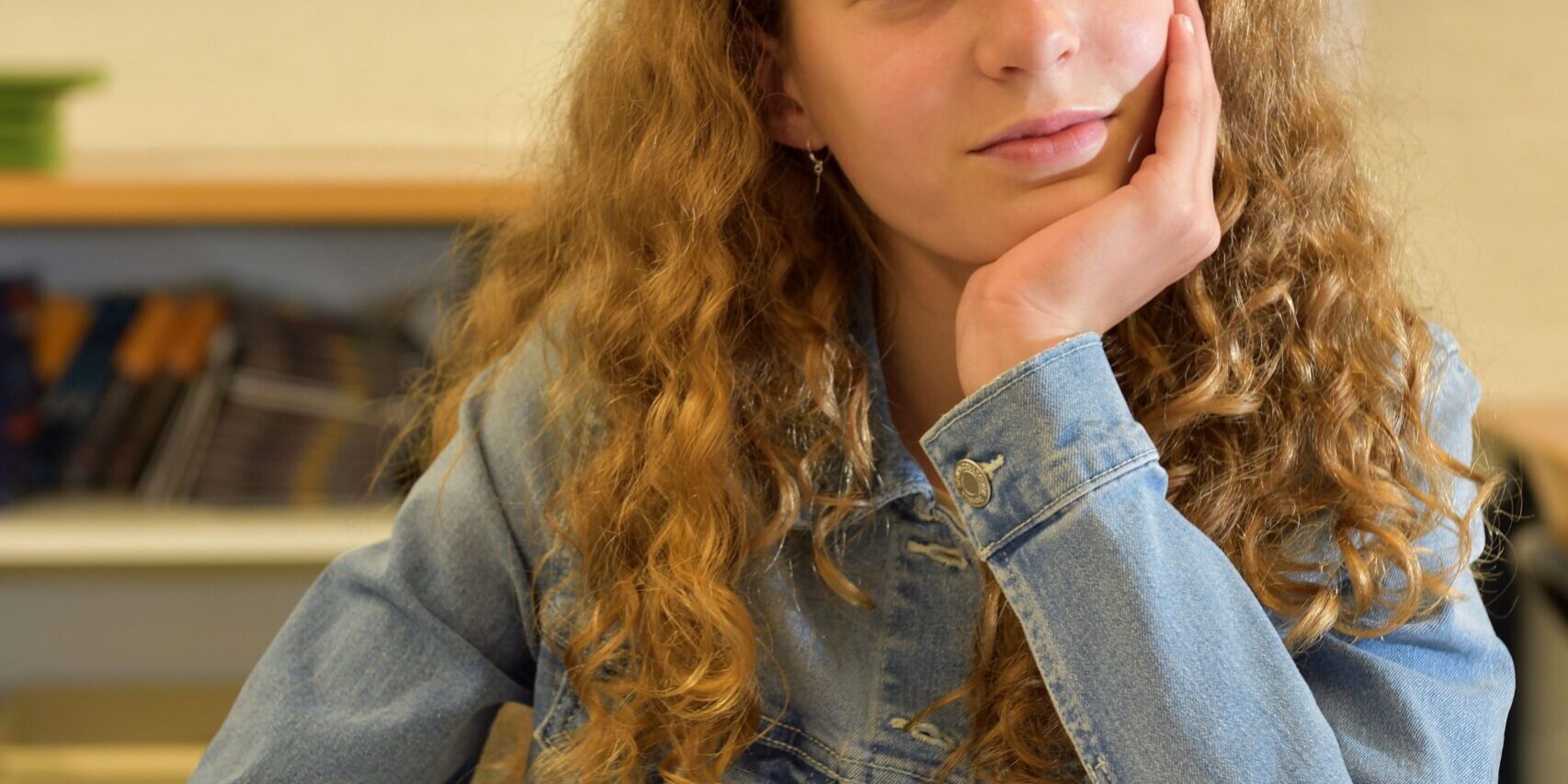 Studentessa riflette su come scegliere le scuole superiori Una studentessa con i capelli rossi e ricci guarda fuori dalla finestra sorridendo.